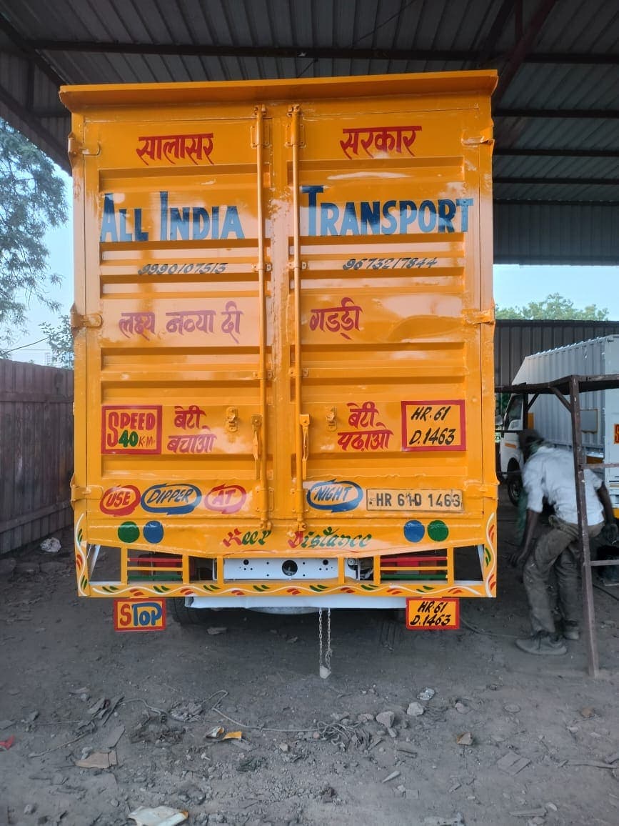 Indian movers loading sturdy cardboard boxes into the back of a large covered transport container truck